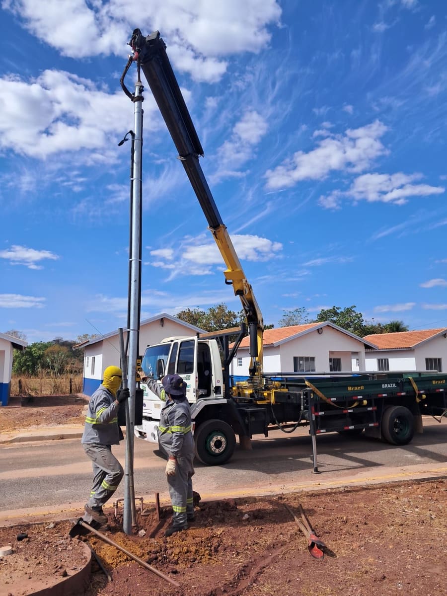 Equipe com equipamento de proteção posicionando poste içado pelo munck