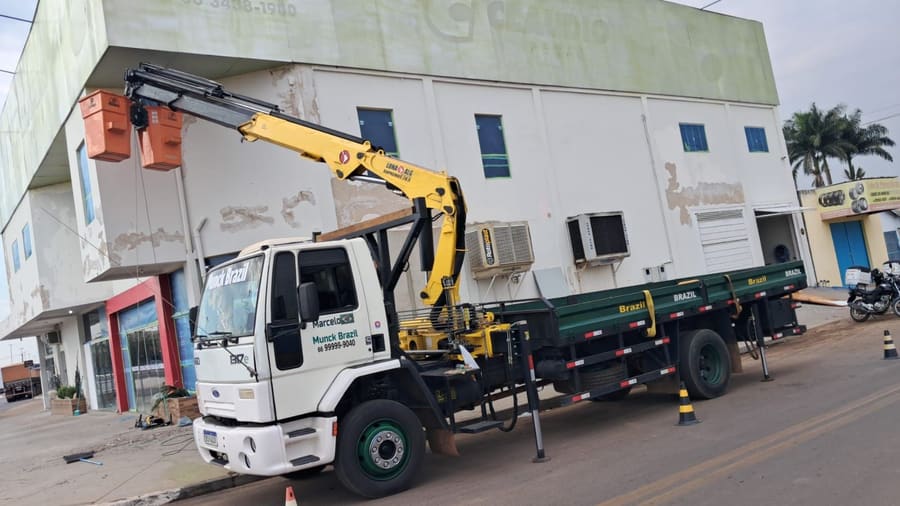 Caminhão munck da Munck Brazil içando equipamentos de ar-condicionado na fachada de um prédio